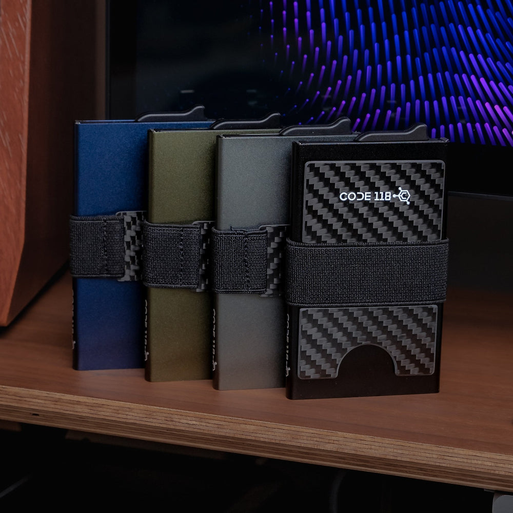 Four CODE 118 Wallets in navy, green, gray and carbon fiber, each with its cash strap, on a desk shelf