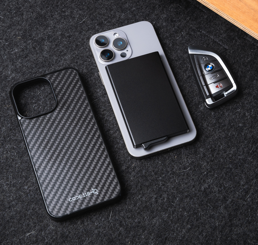 Black CODE118 Wallet for MagSafe attached to a phone beside a phone case and keys