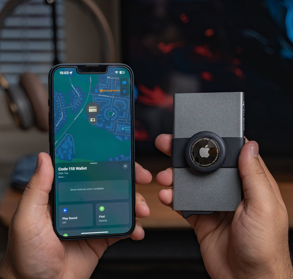 Hands holding a CODE 118 wallet with an AirTag Strap beside an iPhone showing the wallet in Find My