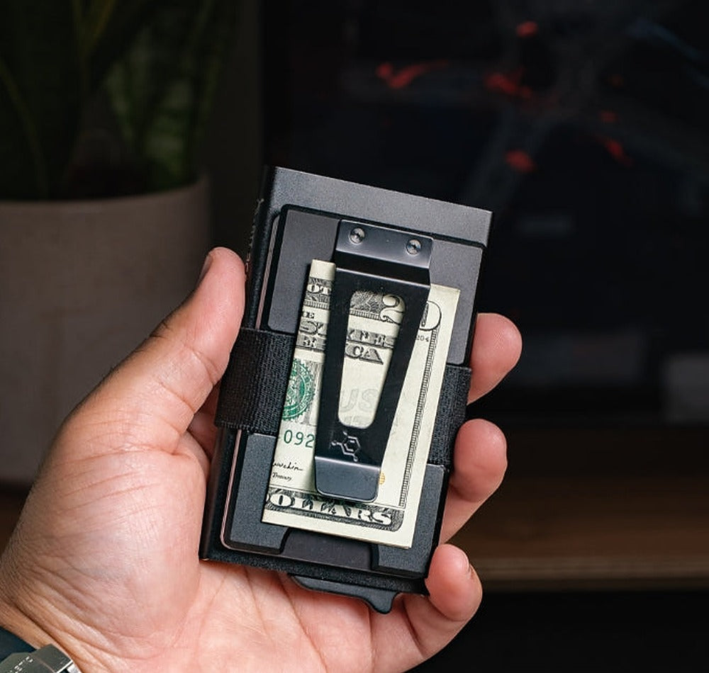 CODE118 Cash Clip Backplate in Black Aluminum installed on a wallet held in a hand with folded cash secured under the clip