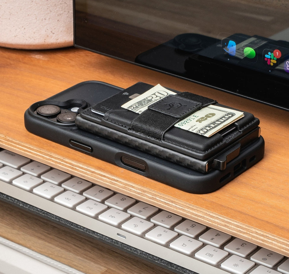 Black CODE 118 Mag Pouch with cash and a card on a MagSafe phone, sitting on a wooden desk shelf above a keyboard