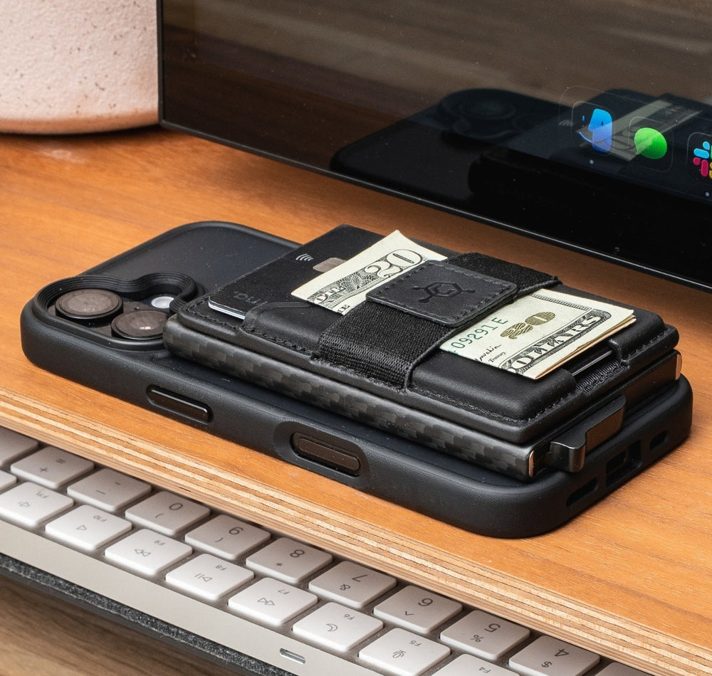 Black CODE 118 Mag Pouch with cash and a card on a MagSafe phone, sitting on a wooden desk shelf above a keyboard