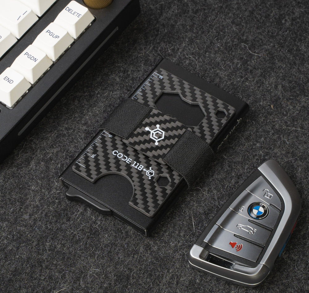 CODE 118 wallet with a carbon fiber Multi-Tool Card under the strap, next to a keyboard and a car key