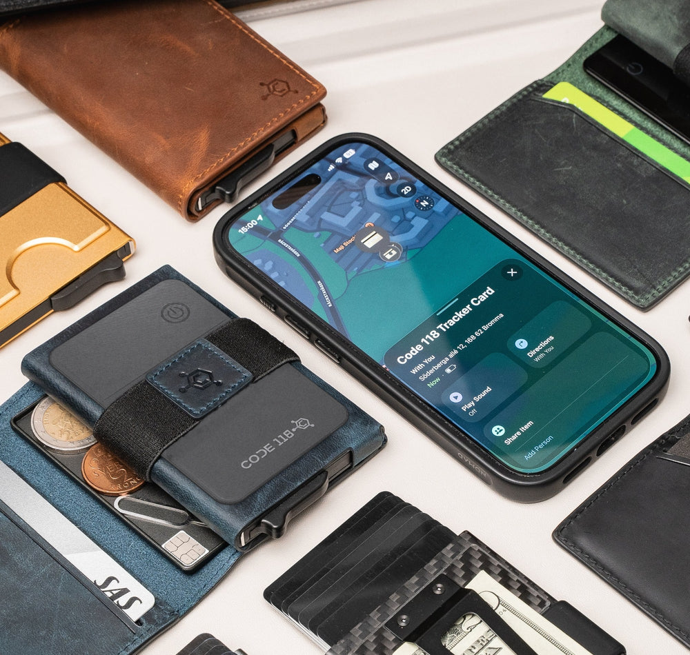 Flat lay of CODE 118 wallets and add-ons around a phone showing the Tracker Card in Find My